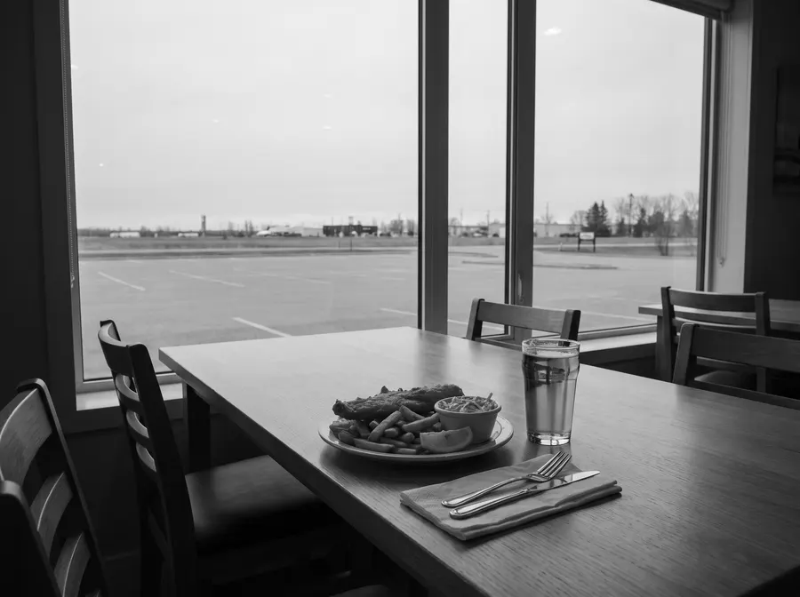 Generated black-and-white scene: fish and chips, coleslaw and a glass of lager on a restaurant table by a window; not a photograph of Kihiw or the Deli & Bar.